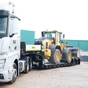 LKW mit Tieflader-Anhäger von DOLL, auf dem ein Baustellenfahrzeug geladen ist, fährt eine Kurve